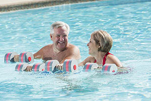 Woman and man doing water aerobics with weights in pool.