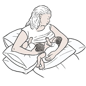 Woman breastfeeding twins with combination football and cradle holds.