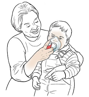 Woman holding toddler on lap and helping him breathe through mask with metered-dose inhaler.