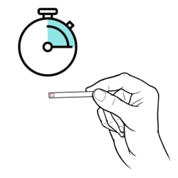 Hand holding ketone test strip and waiting for results to show.