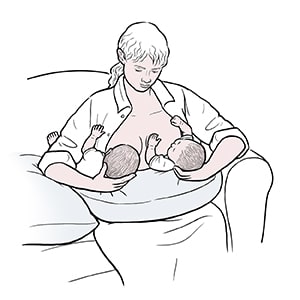 Woman breastfeeding twins with double football hold.