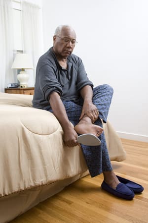 Person sitting on edge of bed looking at sole of foot with mirror.