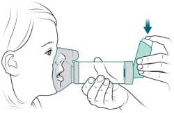 Person pressing down on inhaler to spray medicine into spacer.