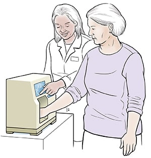 Healthcare provider giving woman bone density test. Woman's hand is in small machine.